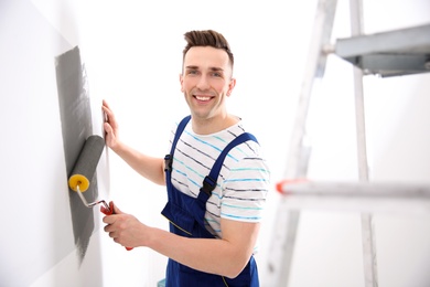 Young male decorator painting wall in room
