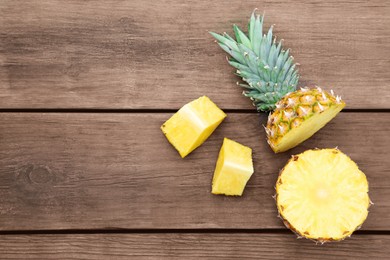 Photo of Cut ripe pineapple on wooden table, flat lay. Space for text