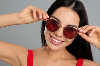 Photo of Beautiful woman wearing sunglasses on grey background, closeup
