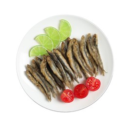 Plate with delicious fried anchovies, lime slices and tomatoes on white background, top view