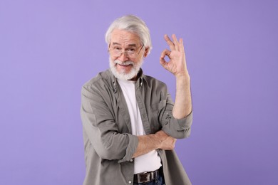 Photo of Portrait of stylish grandpa with glasses showing ok gesture on purple background