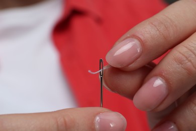 Woman inserting thread through eye of needle, closeup