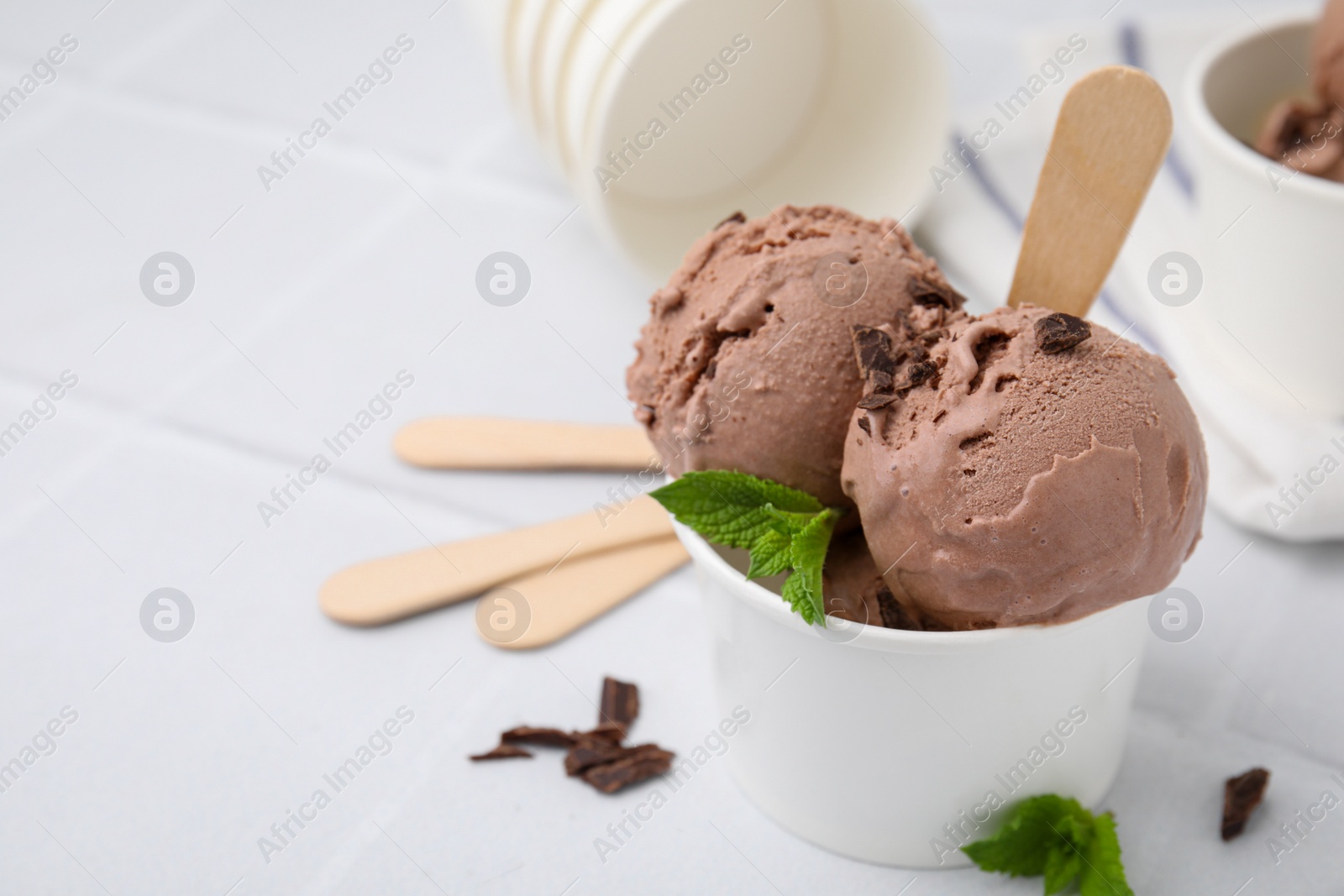 Photo of Paper cups with tasty chocolate ice cream on white tiled table, closeup. Space for text