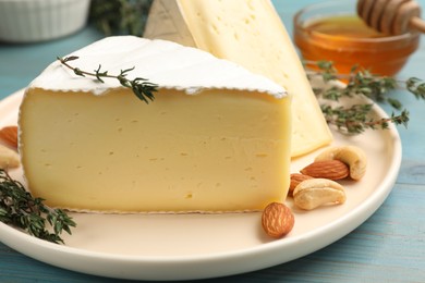 Photo of Tasty Camembert cheese with thyme and nuts on light blue wooden table, closeup