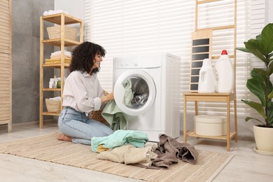 Woman putting laundry into washing machine indoors