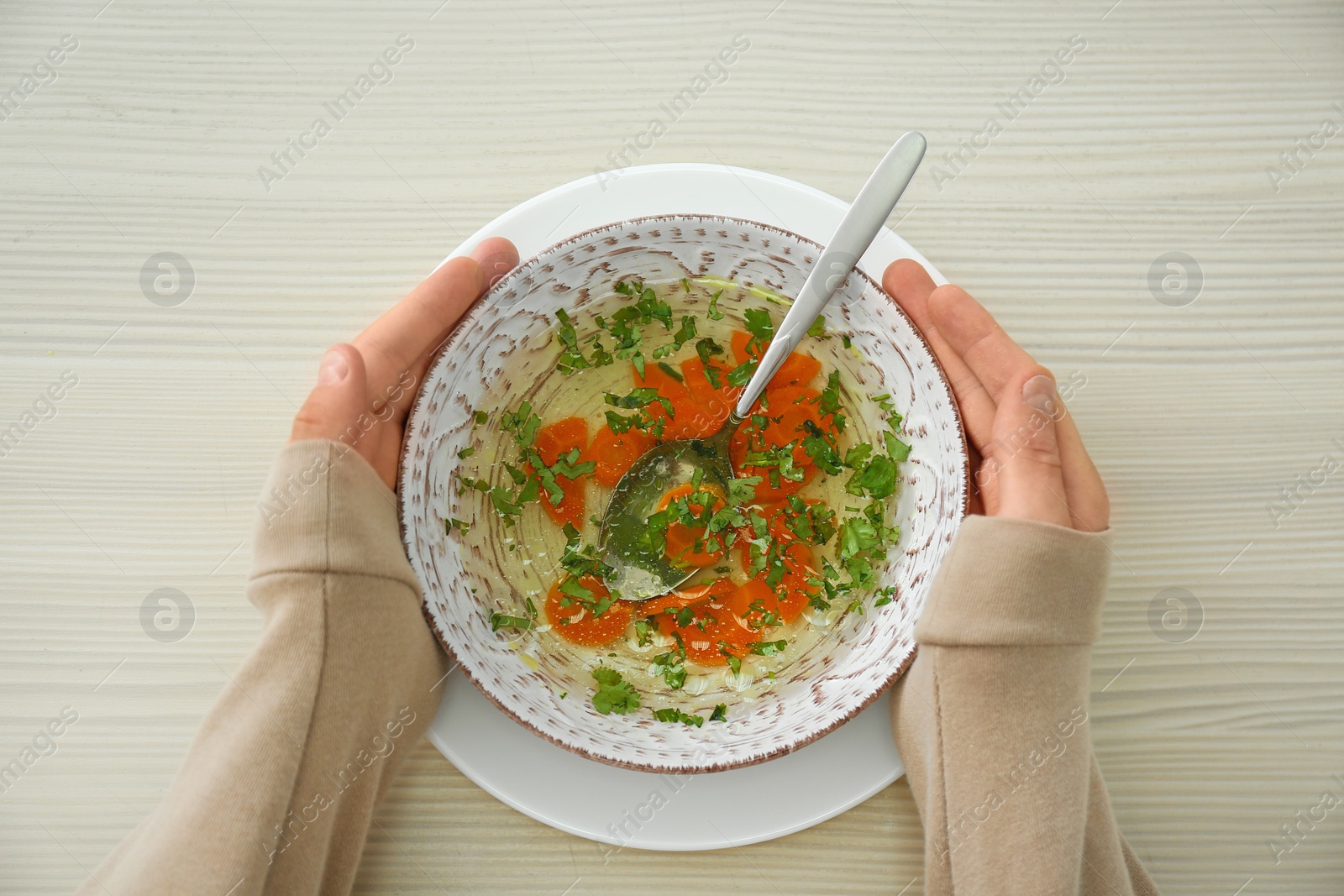 Photo of Man with bowl of soup at wooden table, top view. Flu treatment