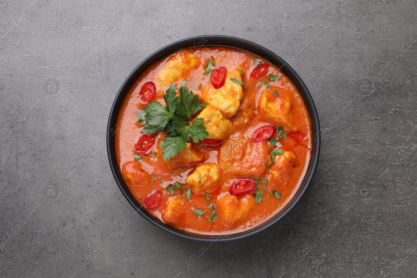 Photo of Bowl of delicious chicken curry on grey table, top view