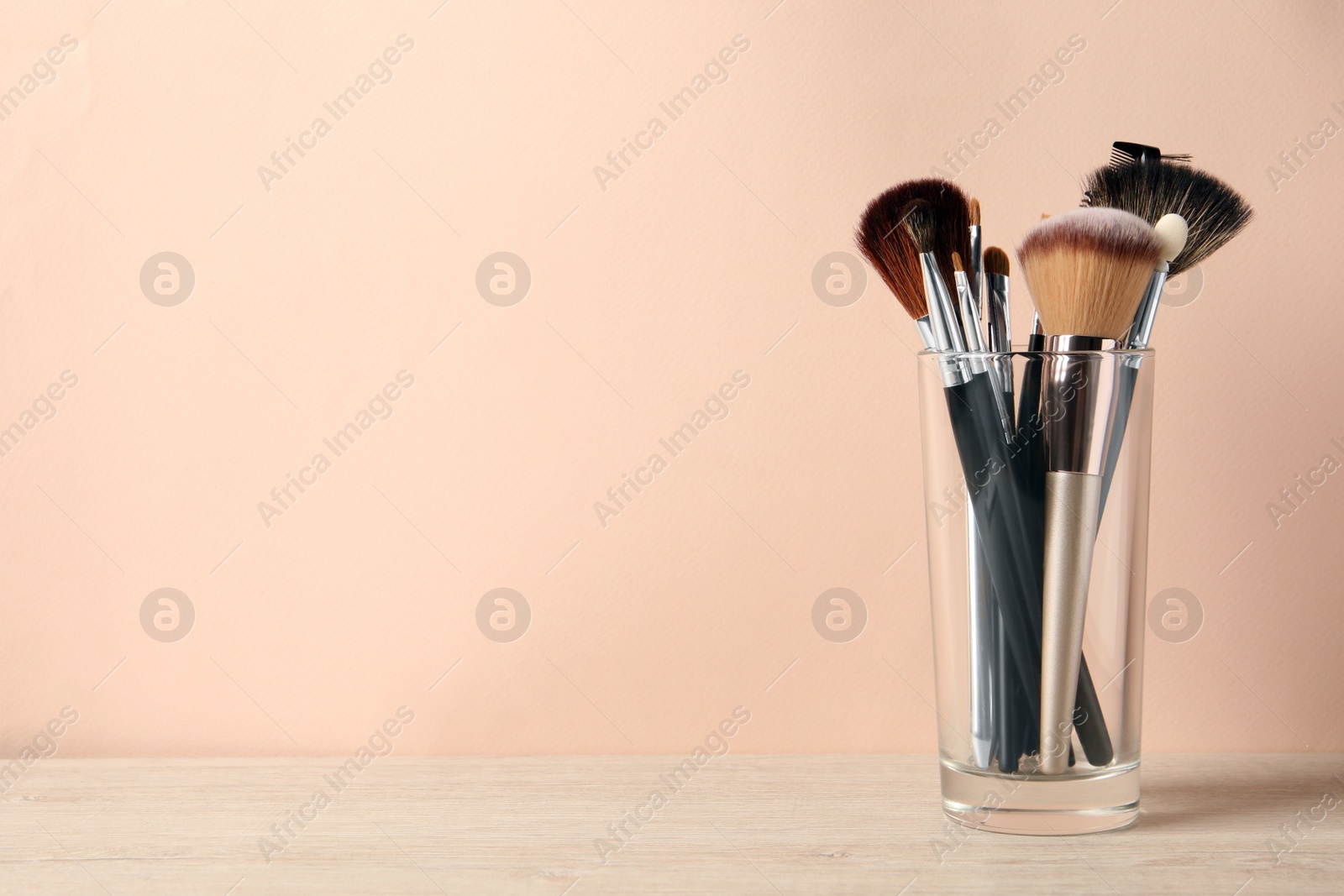 Photo of Set of professional makeup brushes on wooden table against beige background, space for text