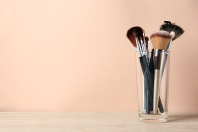 Photo of Set of professional makeup brushes on wooden table against beige background, space for text