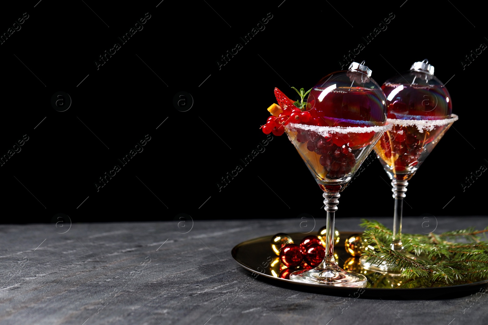 Photo of Creative presentation of Christmas Sangria cocktail in baubles and glasses on grey table against black background. Space for text