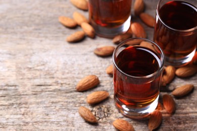 Photo of Shot glasses with tasty amaretto liqueur and almonds on wooden table, closeup. Space for text