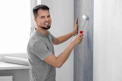 Man hanging stylish gray wallpaper in room