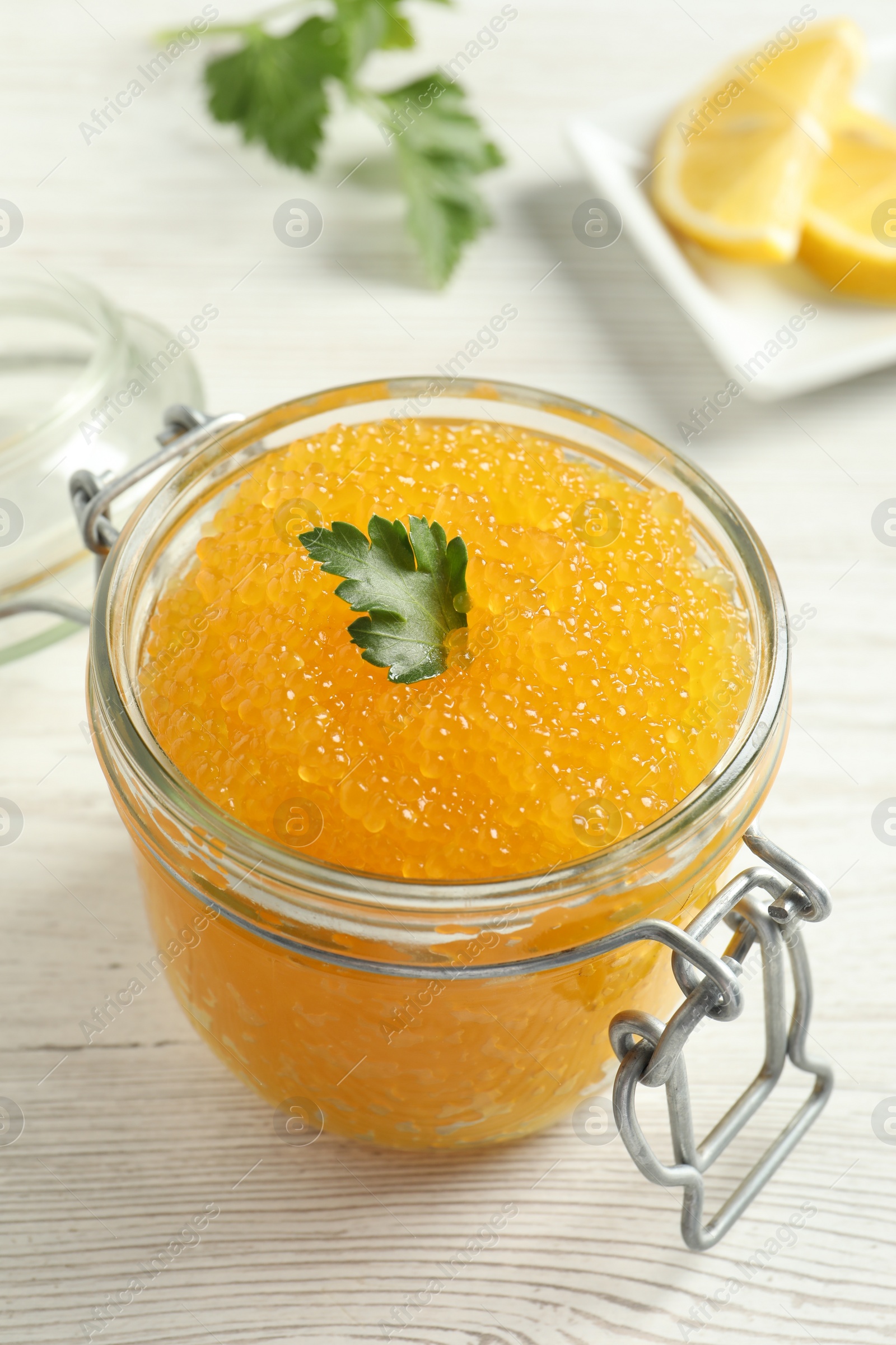 Photo of Fresh pike caviar in glass jar and parsley on light wooden table, closeup