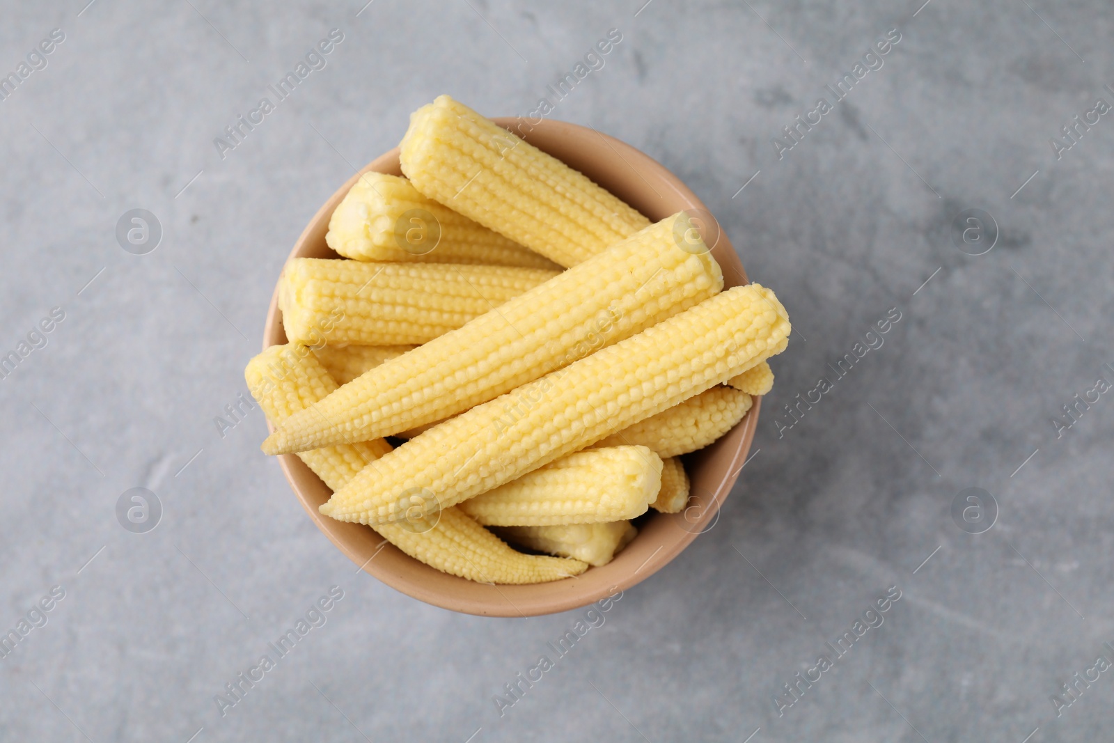 Photo of Tasty fresh yellow baby corns in bowl on grey table, top view