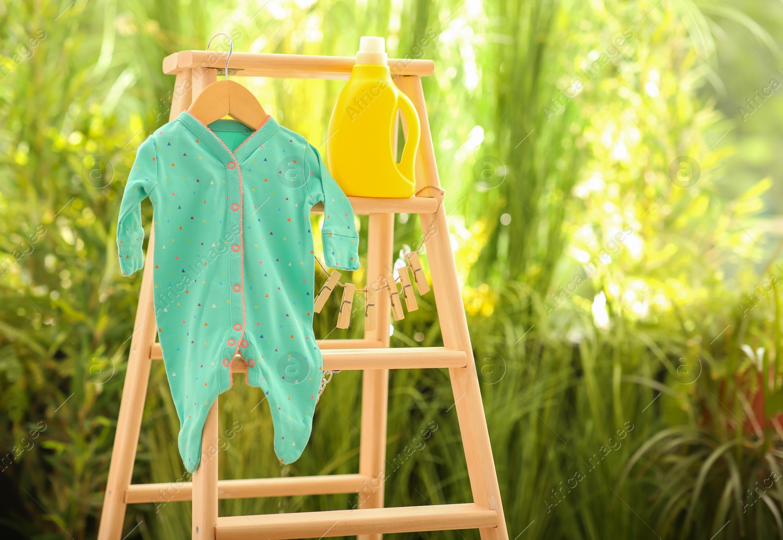 Photo of Bottle of detergent and children's bodysuit on wooden ladder outdoors