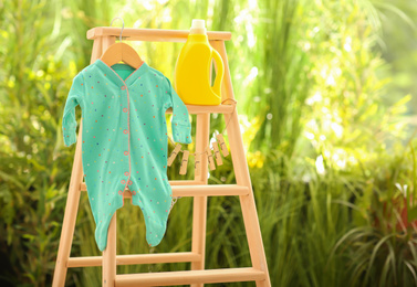 Bottle of detergent and children's bodysuit on wooden ladder outdoors