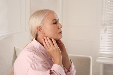 Photo of Mature woman doing thyroid self examination at home, space for text