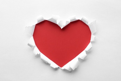 Photo of Torn heart shaped hole in white paper, top view. Red space for text