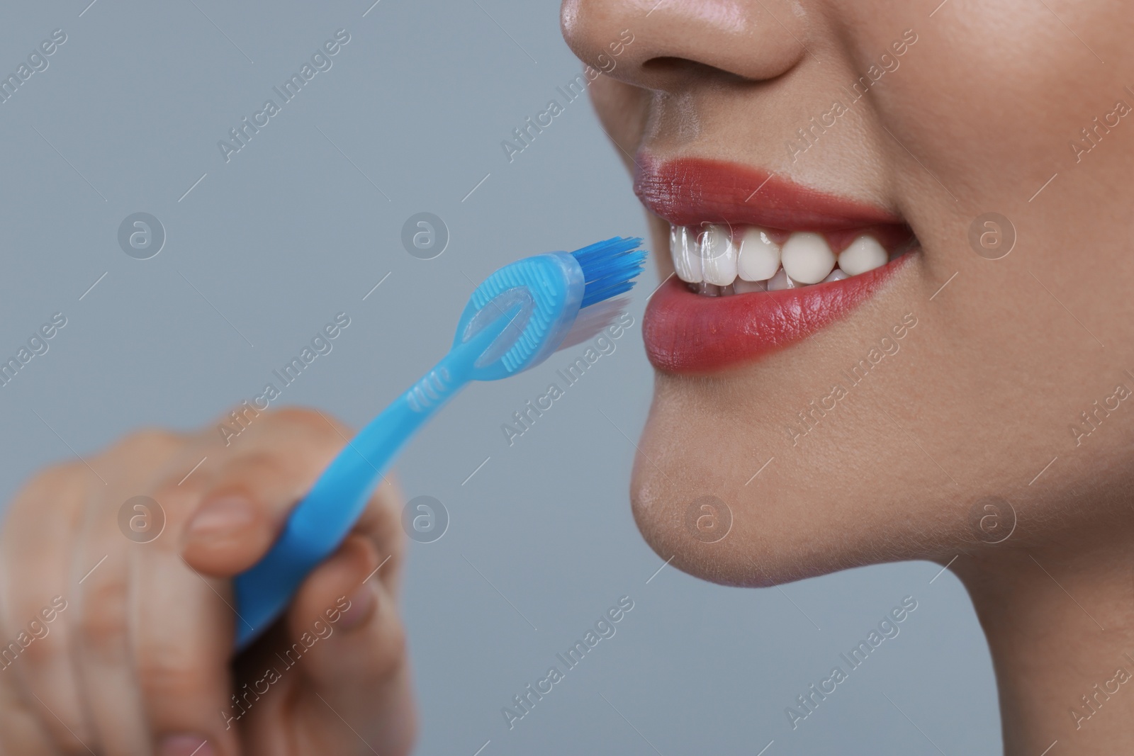 Photo of Woman brushing her teeth with plastic toothbrush on light grey background, closeup