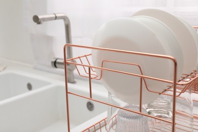 Drying rack with clean dishes near sink in kitchen, closeup
