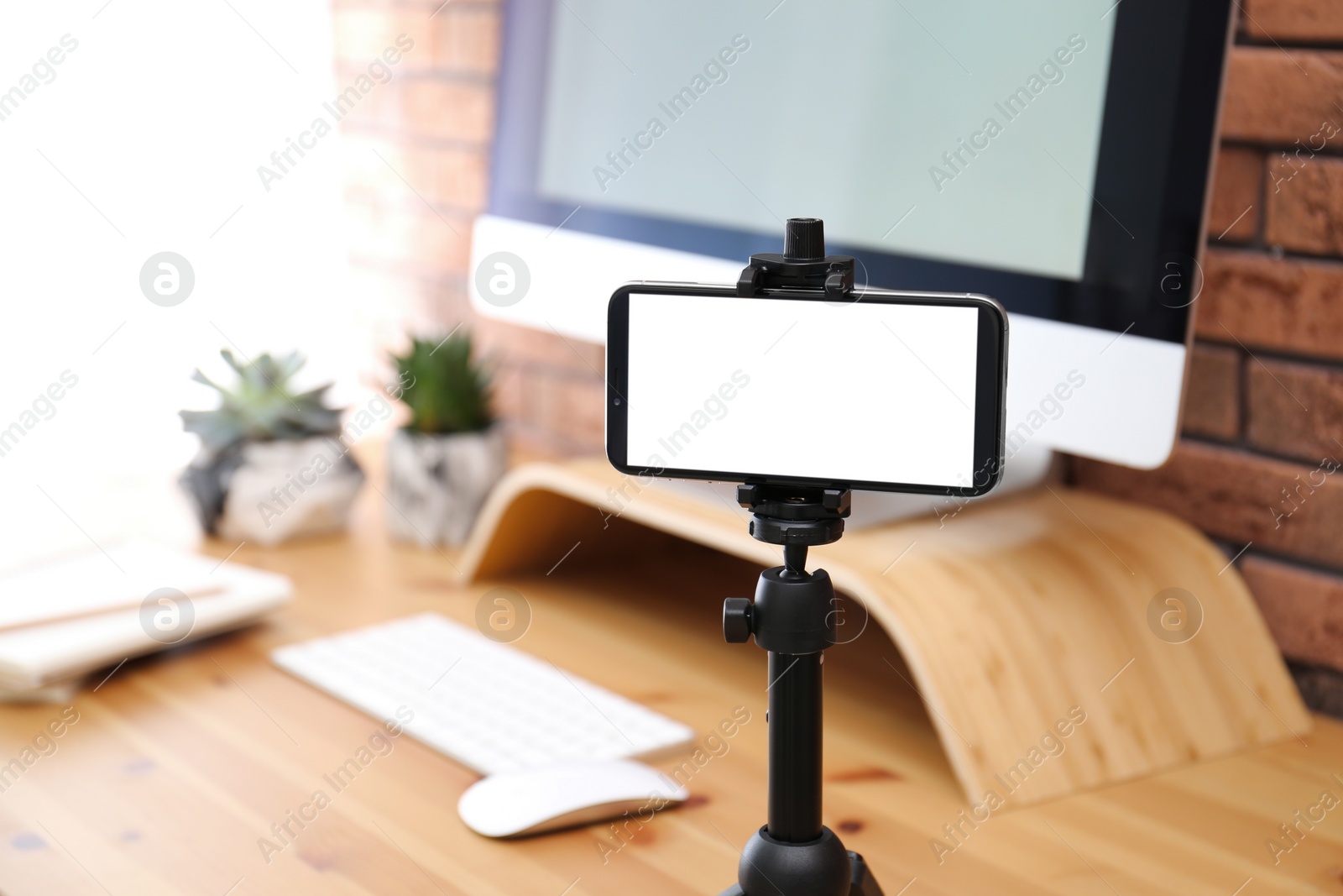 Photo of Stand with smartphone near computer on table indoors. Mockup for design