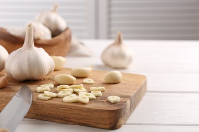 Aromatic cut garlic, cloves and bulbs on white wooden table, closeup. Space for text