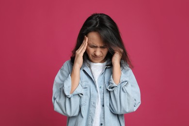 Mature woman suffering from headache on pink background