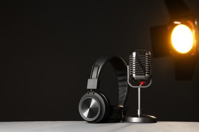 Photo of Vintage microphone and headphones on table against black background, space for text. Sound recording and reinforcement