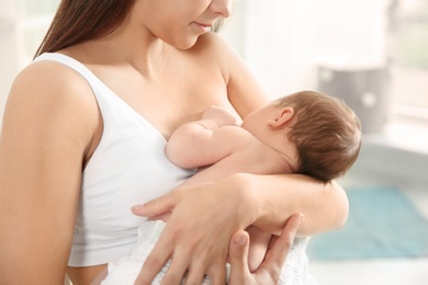 Young woman breastfeeding her baby on blurred background, closeup