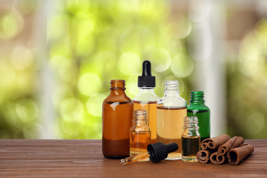 Image of Bottles of essential oils and cinnamon sticks on wooden table against blurred background