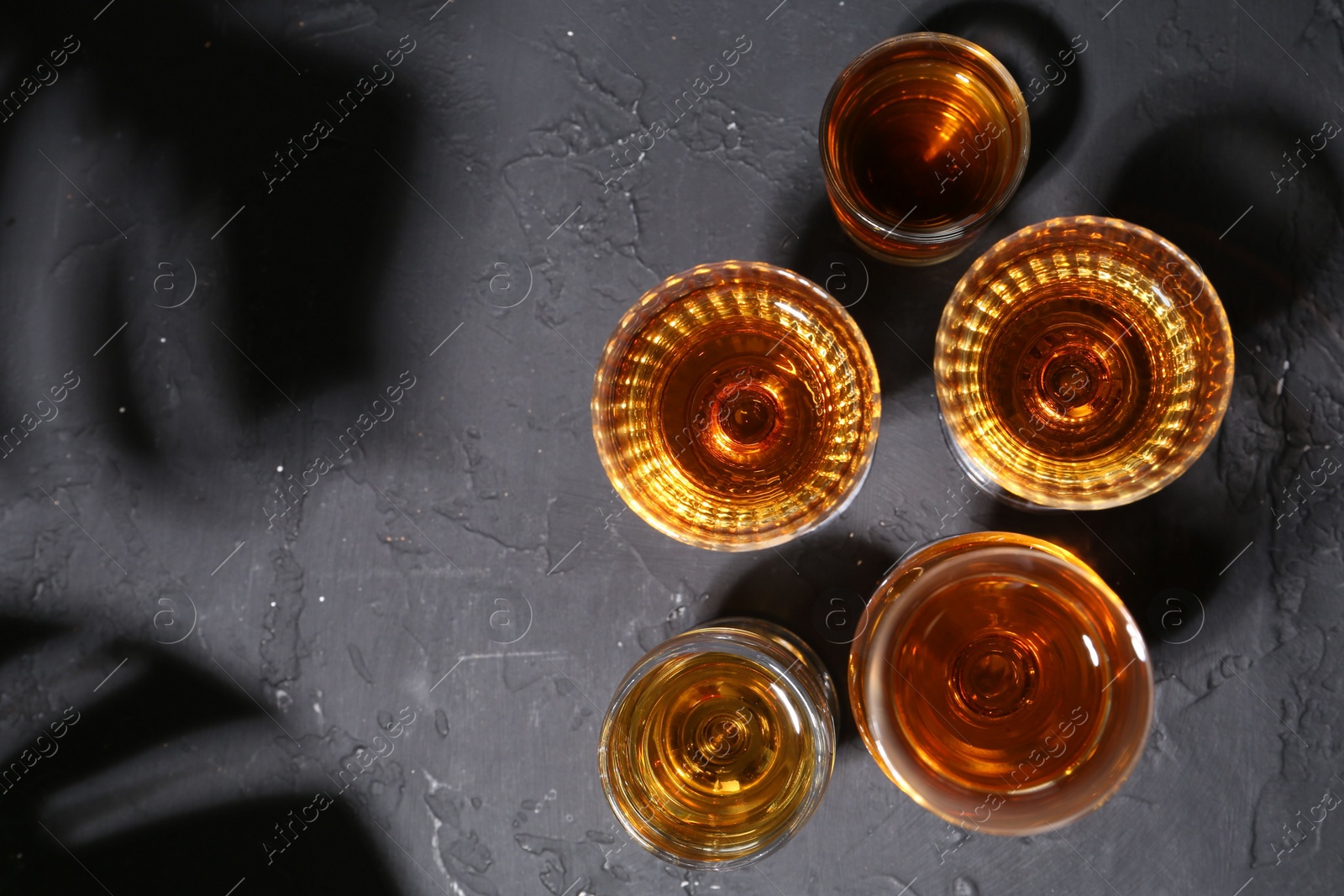 Photo of Many different liqueurs in glasses on dark textured table, flat lay. Space for text