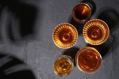 Many different liqueurs in glasses on dark textured table, flat lay. Space for text