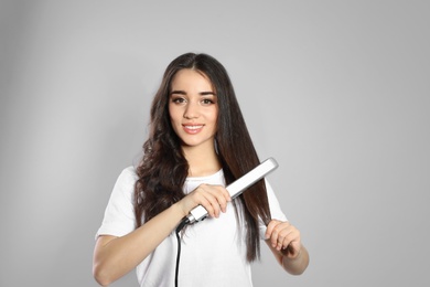 Happy woman using hair iron on grey background