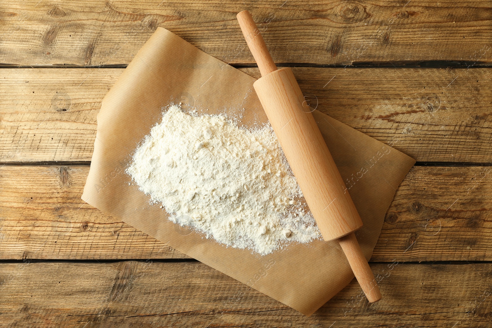 Photo of Parchment with flour and rolling pin on wooden table, top view