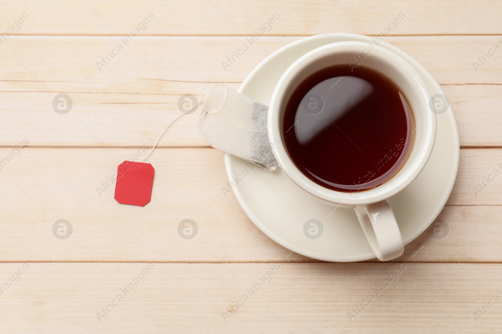 Photo of Tea bag and cup of hot beverage on light wooden table, top view