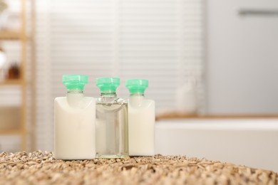 Photo of Mini bottles of cosmetic products on wicker mat against blurred background. Space for text