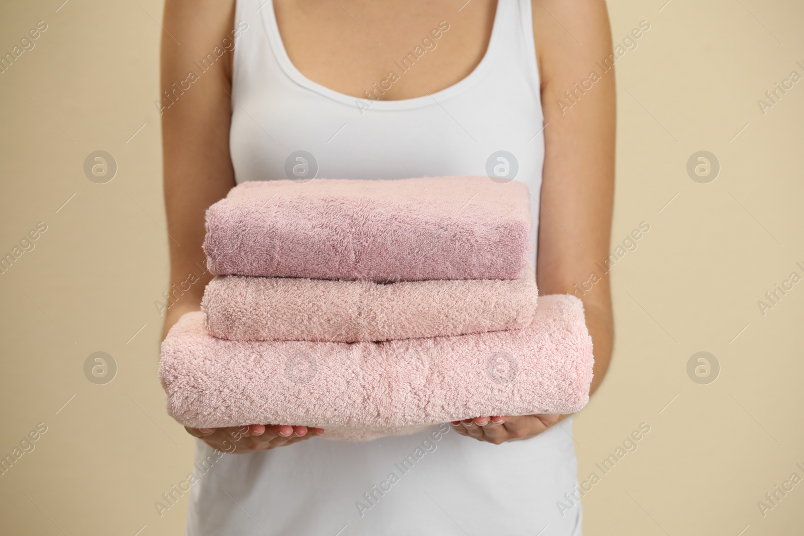 Photo of Woman holding fresh towels on beige background, closeup