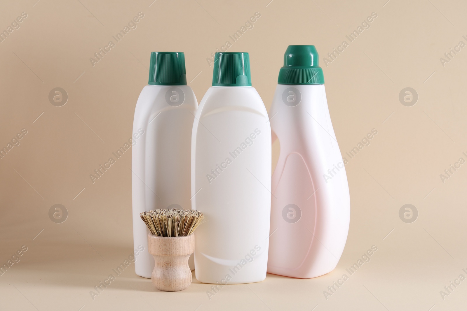 Photo of Bottles of cleaning product and brush on beige background