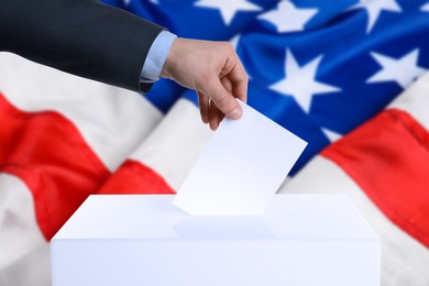 Image of Election in USA. Man putting his vote into ballot box and American flag on background, closeup