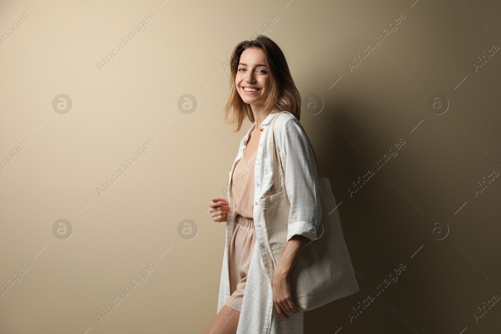 Photo of Happy young woman with blank eco friendly bag against beige background