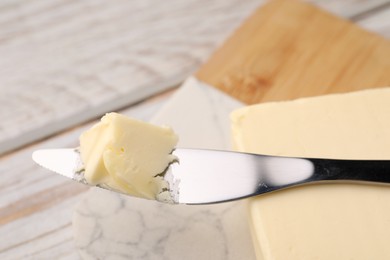 Photo of Tasty butter and knife on white wooden table, closeup