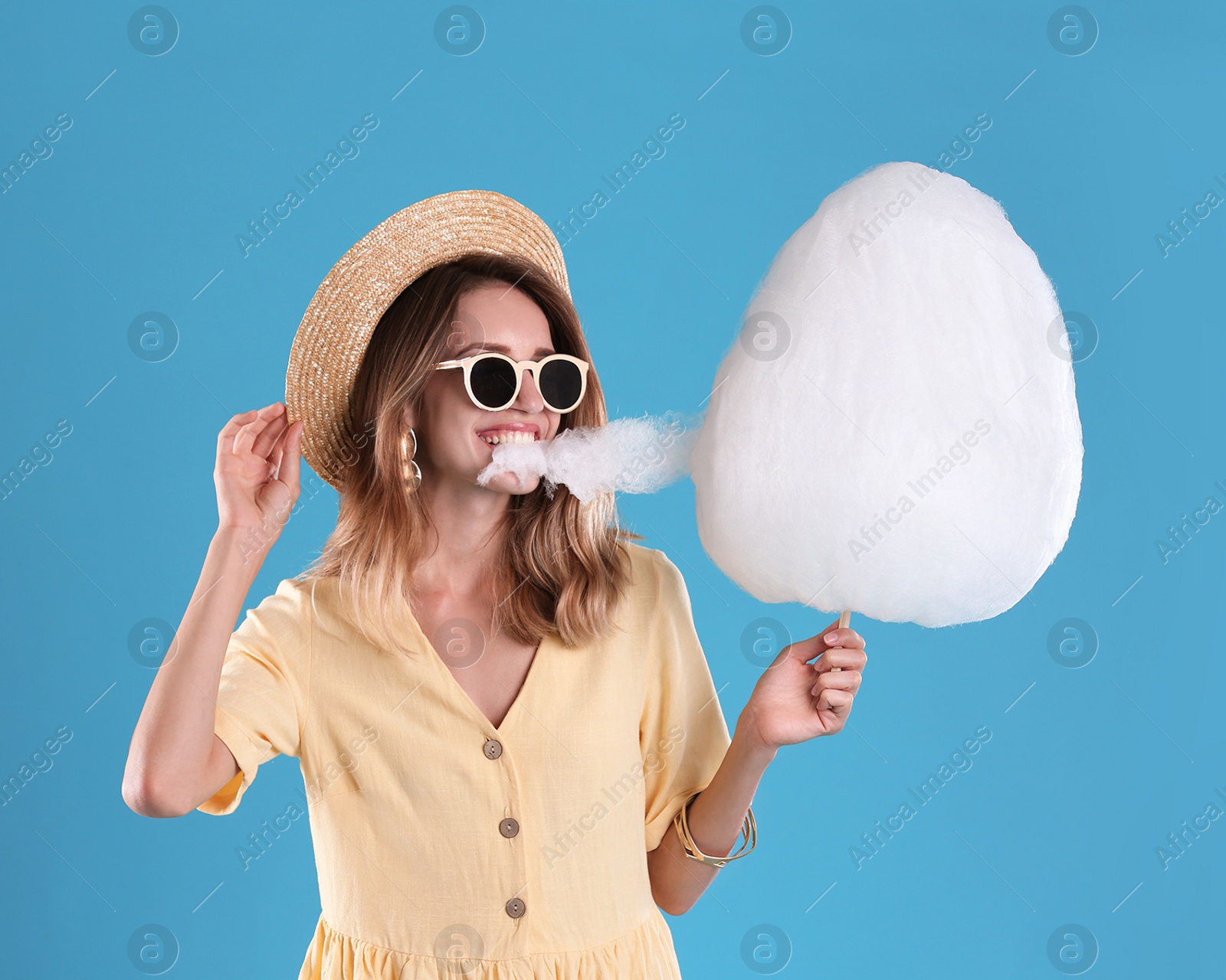 Photo of Happy young woman eating cotton candy on blue background