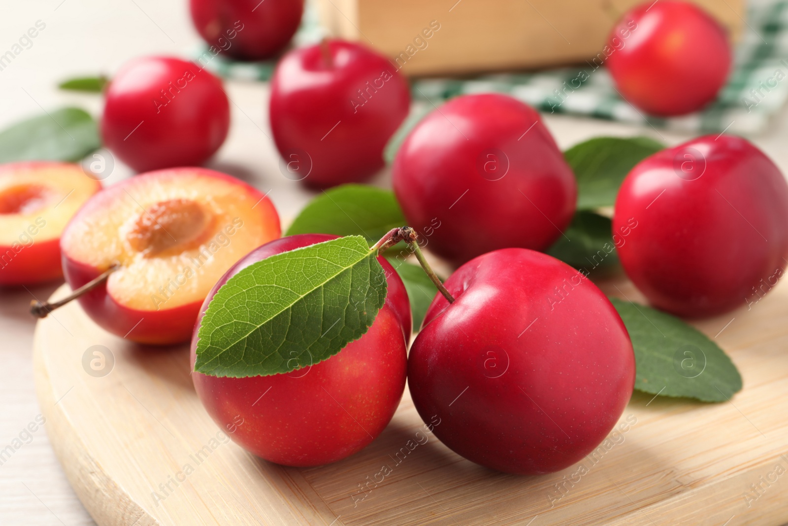 Photo of Delicious ripe cherry plums with leaves on wooden board, closeup