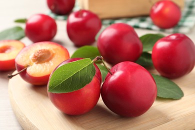 Photo of Delicious ripe cherry plums with leaves on wooden board, closeup