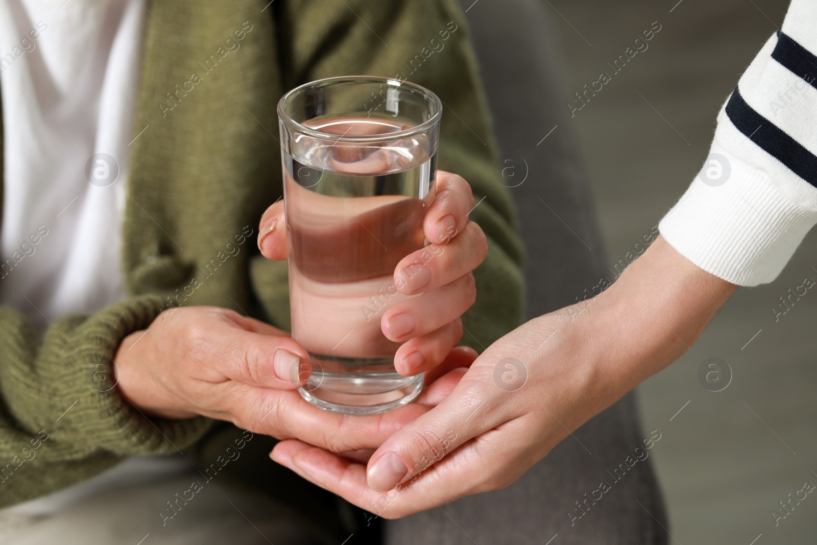 Photo of Caregiver giving water to elderly woman at home, closeup