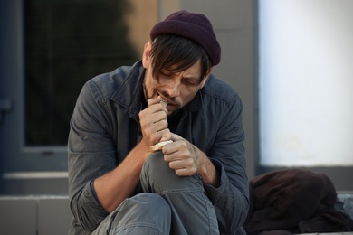 Photo of Poor homeless man eating piece of bread on city street
