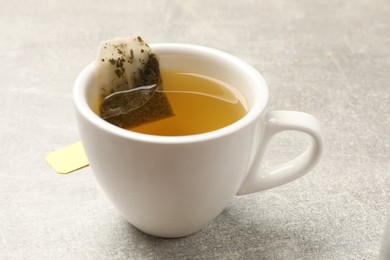 Photo of Brewing tea. Cup with tea bag on light table, closeup