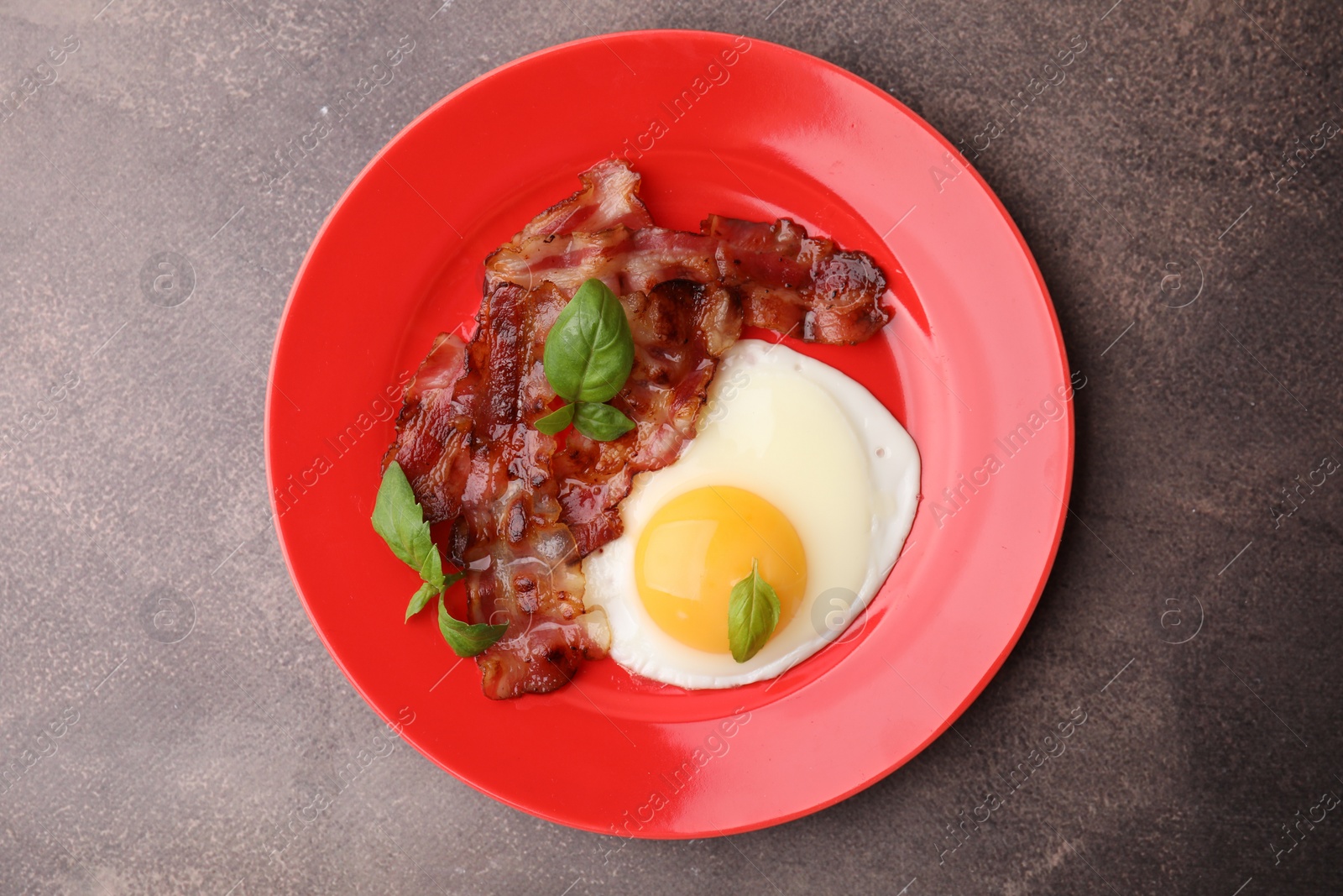 Photo of Fried egg, bacon and basil on brown table, top view