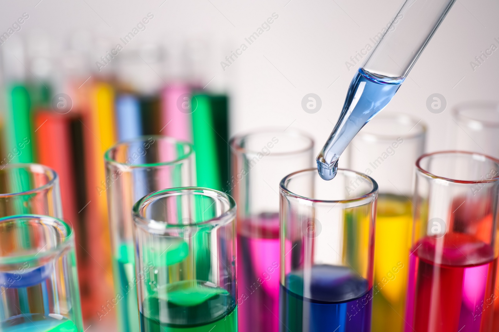 Photo of Dripping liquid from pipette into test tube on grey background, closeup