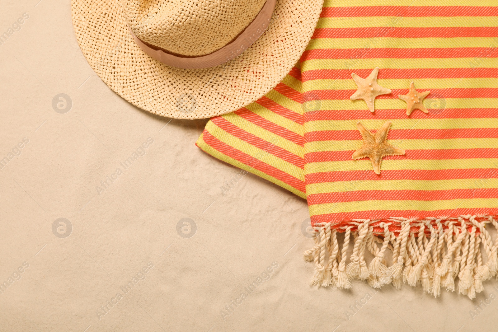 Photo of Beach towel, hat and starfishes on sand, flat lay. Space for text